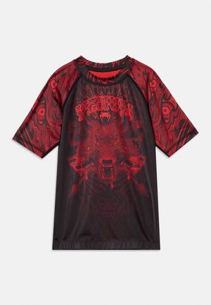 Must ja punane lühikese varrukaga särk, millel on graafiline kujutis kolmekeelsest hundist, nooled ja stiliseeritud mustrid varrukatel ja rinnakohal.