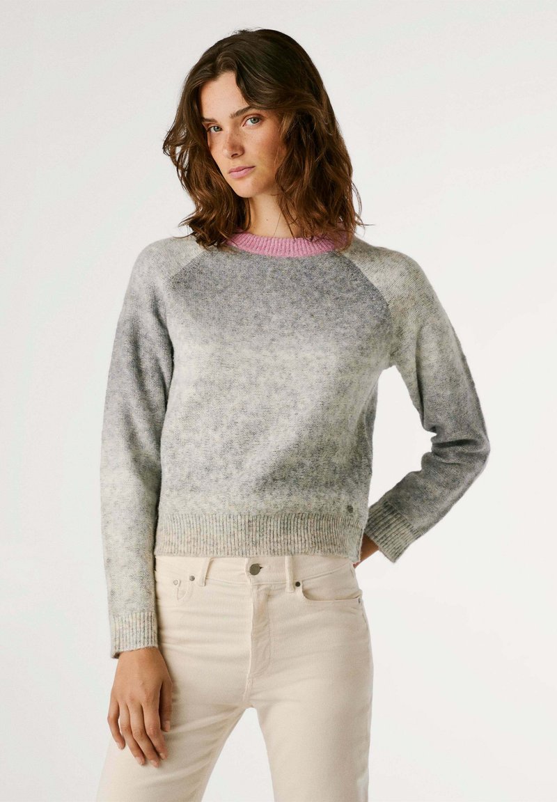 Suéter de lana gris con cuello rosa, mangas raglán y dobladillo acanalado. Textura suave con un patrón de color degradado, combinado con pantalones color blanco roto.
