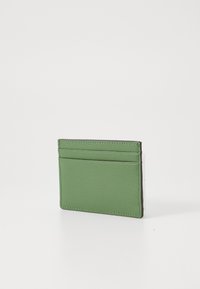 Porte-cartes en cuir vert avec une surface texturée, comportant quatre fentes pour cartes et un profil mince. Les bords sont finis avec une couture contrastante.