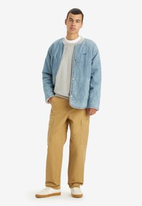 Light blue quilted jacket with a round collar and snap buttons, grey sweatshirt underneath, tan cargo pants, and white sneakers.