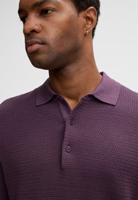 Polo shirt in prugna a maglia con apertura a bottoni, motivo testurizzato e colletto classico. Tessuto liscio con delicata coste sul bordo del colletto.