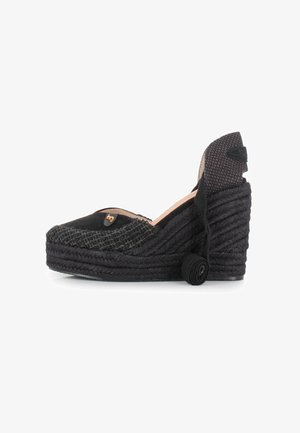 Espadrille de cuña negra con detalles de yute trenzado, punta redonda y tacón cubierto de tela. Presenta un emblema decorativo en la parte delantera.