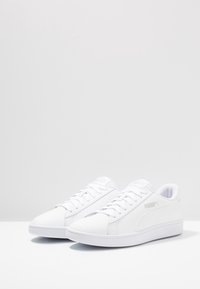 Sneakers bianchi con una superficie liscia e sleek. Caratteristiche includono chiusura con lacci, colletto imbottito e accenti grigi del logo sul lato.