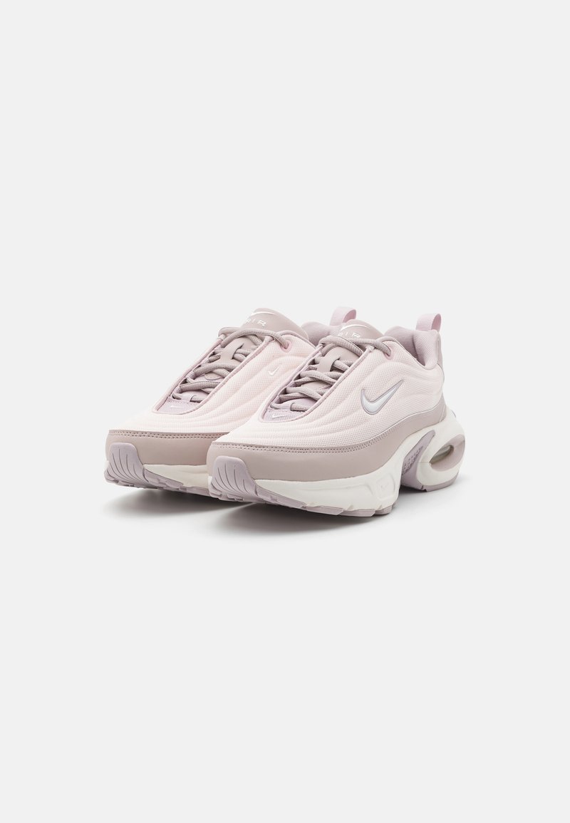 Zapatillas Nike con parte superior de malla rosa claro, acentos grises, puntera redondeada y amortiguación de aire visible en la suela. Cordones en colores a juego.