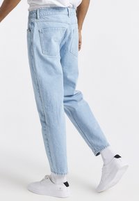 Jeans de mezclilla azul claro con un corte relajado, que cuentan con dos bolsillos traseros y bajos remangados. Combinados con zapatillas blancas y calcetines grises.