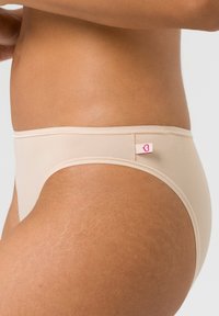 Beige Baumwollslip mit glatter Textur, im niedrigen Schnitt und einem kleinen pinken Logo-Tag an der Seite. Schlichtes, minimalistisches Design.