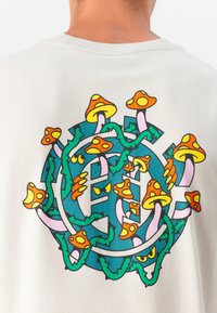 Kreminė medvilninė marškinė su spalvinga grybų grafika, susipynusia su žaliomis vijokliais. Dizainas apima oranžinius, rožinius ir mėlynus akcentus.