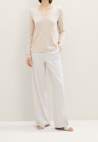 Hellbeiger V-Ausschnitt-Pullover mit langen Ärmeln, kombiniert mit weißen weit geschnittenen Hosen. Das Outfit wird durch beige Slipper-Sandalen ergänzt.