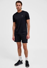 Svart atletisk t-shirt och shorts med en slät yta; logotypdetalj på bröstet och sidan av shortsen; bärs med svarta sneakers och vita strumpor.