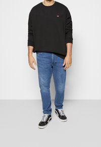 Sweat-shirt noir à col rond avec logo Levi's, jean bleu et baskets Vans noires avec lacets blancs. Coupe décontractée standard, design simple.