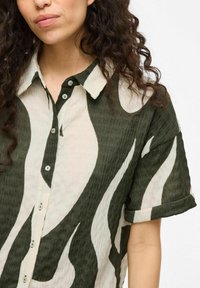 Button-up shirt featuring a green and off-white wave pattern, made of textured fabric with a foldable collar and short sleeves.