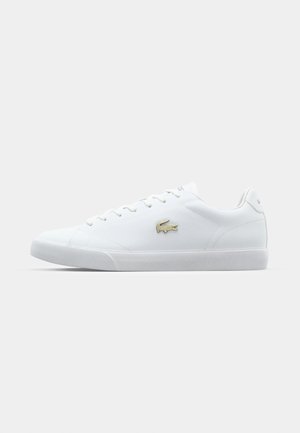 Sneaker bianca con finitura in pelle liscia, dotata di una suola in gomma testurizzata, lacci piatti e un logo ricamato dorato sul lato.