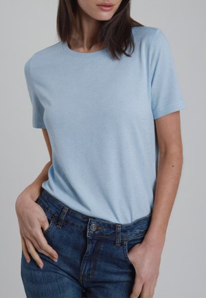 Donna che indossa una maglietta a maniche corte azzurro chiaro infilata in jeans di jeans blu scuro con le mani nelle tasche.