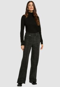 Un haut à col roulé noir associé à un pantalon large à motifs sombres. Présente un design texturé et de subtils accents en métal.