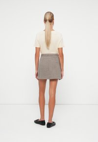 T-shirt beige, gonna corta a quadri grigia con vita cinturata e scarpe basse nere. Tessuto morbido, design semplice.