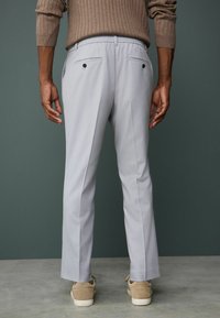 Light gray trousers with a relaxed fit, featuring a ribbed waistband and two back pockets with black buttons, worn with beige sneakers.