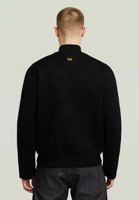 Maglione nero con collo alto, texture a costine e una piccola etichetta del marchio sul retro. Presenta maniche lunghe e una vestibilità comoda.