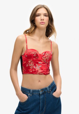 Red satin bustier with embroidery, featuring thin straps and a cropped design. Paired with high-waisted blue denim shorts.