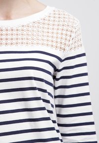 Randig topp i vitt och marinblått med en texturerad spetskjol. Tillverkad av mjukt tyg, med långa ärmar och en avslappnad passform.