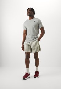 Gray short-sleeve t-shirt with black logo, striped olive shorts, white crew socks, and red athletic shoes with black accents.