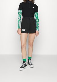 Black ribbed zip-up top with short sleeves and green floral patterned long sleeves, paired with black shorts featuring a white logo. Black and white boots.