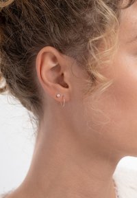 Gouden oorring met een kleine parel als accent, gedragen aan het oor van een model. Benadrukt zachte rondingen en gladde texturen van het metaal en de parel.