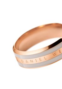 Vaaleanpunakultaiset kellonrannekkeet jossa on valkoinen keraaminen sisustus; siinä on kaiverrettu "DANIEL WELLINGTON", sileä pinta, pyöristetyt reunat ja tyylikäs muotoilu.