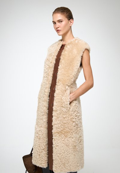 Gilet in pelliccia beige con un'esterno morbido e texturizzato, dotato di fodera interna marrone e tasche laterali, design senza maniche e chiusura frontale con bottoni.