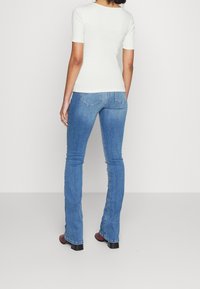 Bílý žebrovaný top s krátkým rukávem, doplněný světle modrými rozšířenými džíny. Džíny mají klasický pětikapsový design a světlé praní.