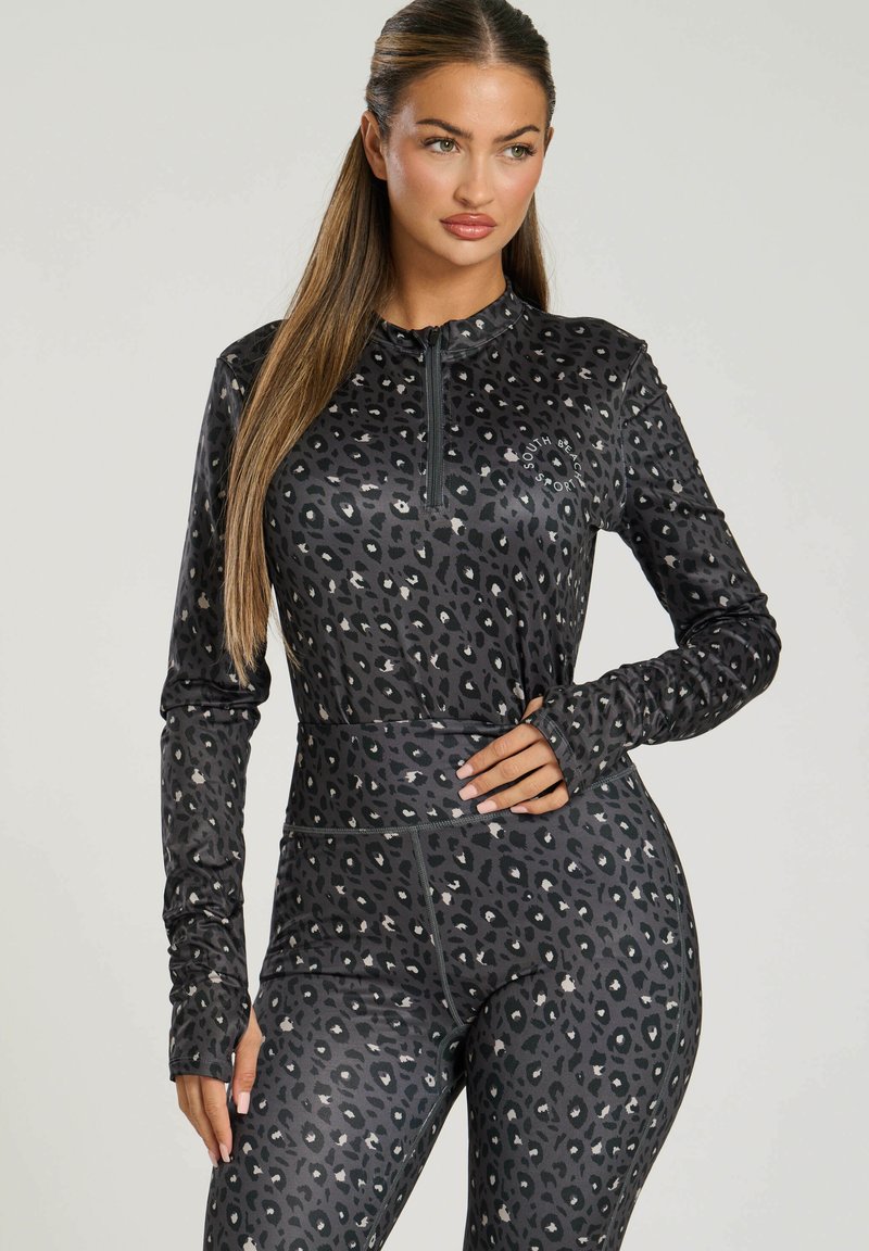 Schwarzes Sportset mit einem Reißverschluss-Oberteil und hochtaillierten Leggings im Leopardenmuster. Glatte Textur und figurnahe Passform.