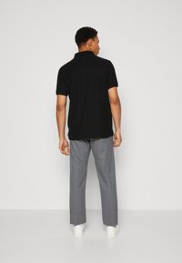 Schwarzes Poloshirt mit weicher Textur, kombiniert mit grauen Anzughosen. Hat einen klassischen Kragen und eine lockere Passform. Weiße Sneakers runden den Look ab.