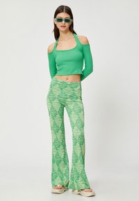 Zielony prążkowany crop top z odkrytymi ramionami, połączony z rozkloszowanymi spodniami z fakturowanym zielonym wzorem. Na nogach lekkie platformowe sandały w jasnym kolorze.