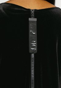 Zwarte fluwelen kleding met een achterrits voorzien van een textured trekstrip met het label "EMPORIO." Gladde textuur en strakke lijnen.