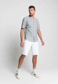 Korte mouwen sporthemd in lichtblauw met abstracte patronen, gecombineerd met witte shorts. Beschikt over een ontspannen pasvorm en lichte stof.