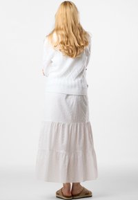Maglione bianco a treccia abbinato a una lunga gonna bianca a strati con un delicato motivo ricamato, completato da sandali beige.
