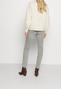 Sudadera beige con mangas abullonadas, jeans ajustados grises y botas de tacón marrones. El atuendo presenta un diseño limpio y minimalista.
