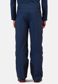 Pantaloni da sci impermeabili di colore navy con vestibilità ampia, sezioni inferiori nere rinforzate e una vita alta per maggiore comfort e flessibilità.