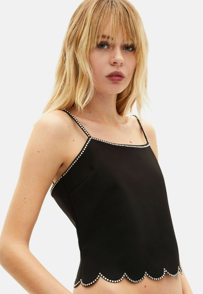 Schwarzes ärmelloses Top mit gewelltem Saum, verziert mit silbernen Nieten entlang des Halsausschnitts und am unteren Rand, glatter Stoff, tailliertes Design.