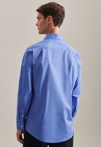 Camicia a maniche lunghe blu chiaro con colletto classico. Presenta polsini con bottoni e un tessuto liscio e testurizzato con una vestibilità strutturata.