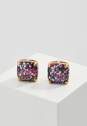 Boucles d'oreilles carrées à clou avec paillettes multicolores encastrées dans des griffes dorées sur un présentoir blanc.
