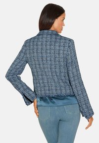 Blauwe tweedjas met een cropped ontwerp, rafelige zoom en lange mouwen. Satijnen onderlaag zichtbaar aan de onderkant. Soepele textuur.