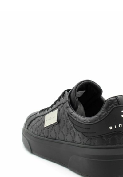 Czarny sneaker z teksturowaną powierzchnią, z prostokątną naszywką z logo i wyściełanym kołnierzem. Gumowa podeszwa i sznurowany design.