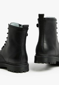 Bottines en cuir noir avec une finition lisse, bout rond, lacets à l'avant et semelle en caoutchouc texturé avec des motifs en relief pour une meilleure adhérence.