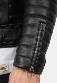 Zwarte leren jasje met een gewatteerde textuur en een ritssluiting bij de manchetten. Met een gladde afwerking en contrasterende metalen ritsaccessoires.