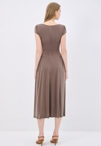 Braunes, knielanges Kleid mit kurzärmligen Ärmeln und einem Reißverschluss hinten. Glatte Textur mit Raffungen an der Taille. Getragen mit braunen Absatzsandalen.