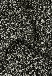 Dzianina w czerni i bieli, ukazująca teksturowany wzór z przeplatanymi niciami, tworząca miękki, ciepły wygląd.