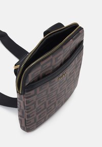 Borsa a tracolla marrone a motivo con zip superiore, dettagli neri e una tasca frontale piatta. Presenta dettagli in metallo dorato e una tracolla regolabile.