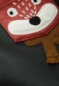 Wzór na haftowanej twarzy zwierzęcia z czerwoną teksturą corduroy i białymi akcentami z pluszu na ciemnym tle; zawiera brązowe akcenty z dzianiny.