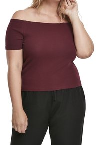 Burgundy off-shoulder-top med korta ärmar, ribbat material och figurnära design, kombinerad med svarta löst sittande byxor.