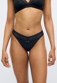 Το μαύρο εσώρουχο διαθέτει ζώνη με κυματιστή δαντέλα και κεντρικό μαύρο φιόγκο, κατασκευασμένο από λεία ύφανση. Κόψιμο εσώρουχου: μπικίνι.